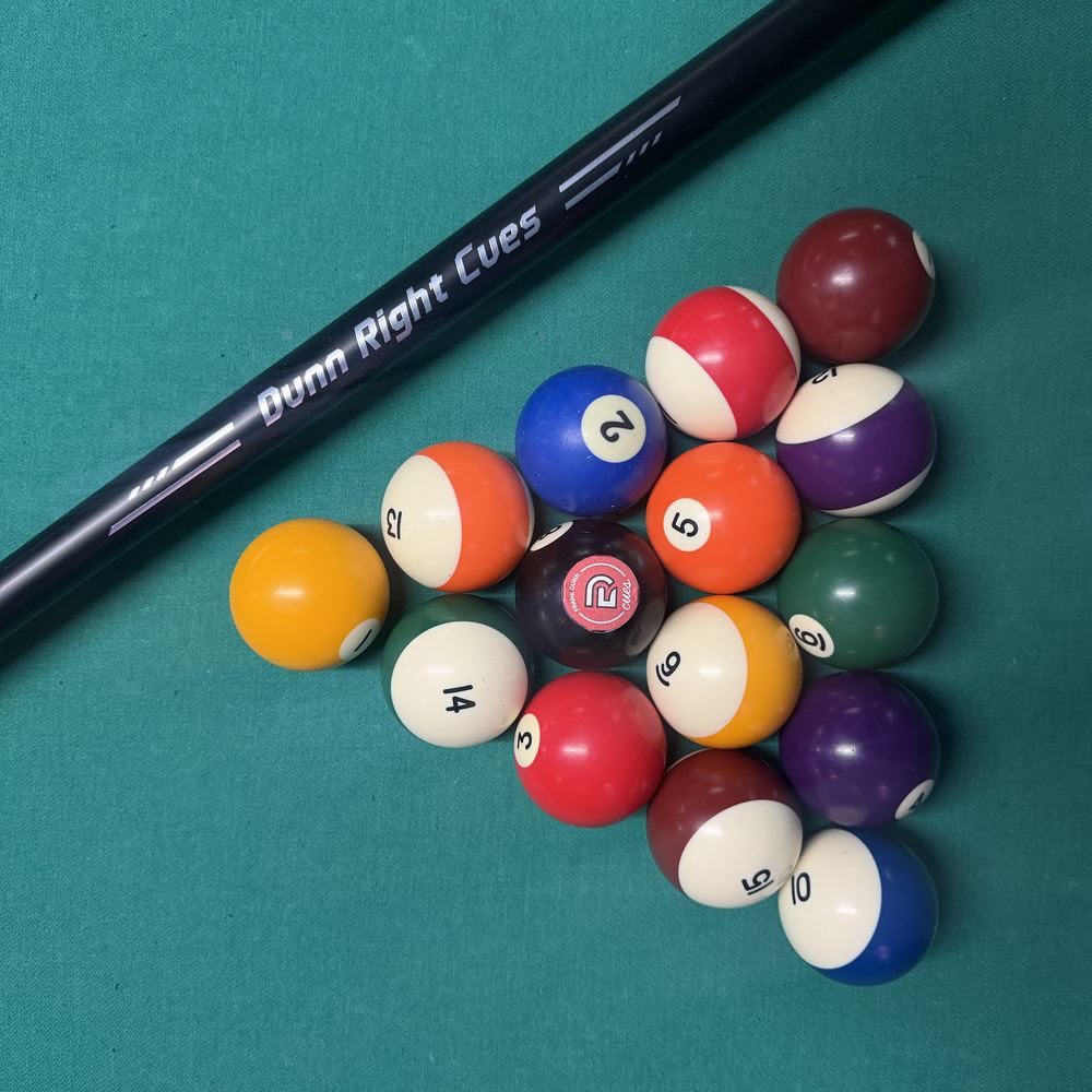 A Dunn Right Cues pool cue resting beside a freshly racked set of billiard balls on a green felt table